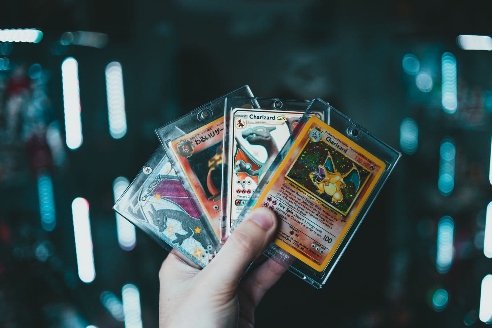 A hand holding four Charizard Pokémon cards in rigid protective holders